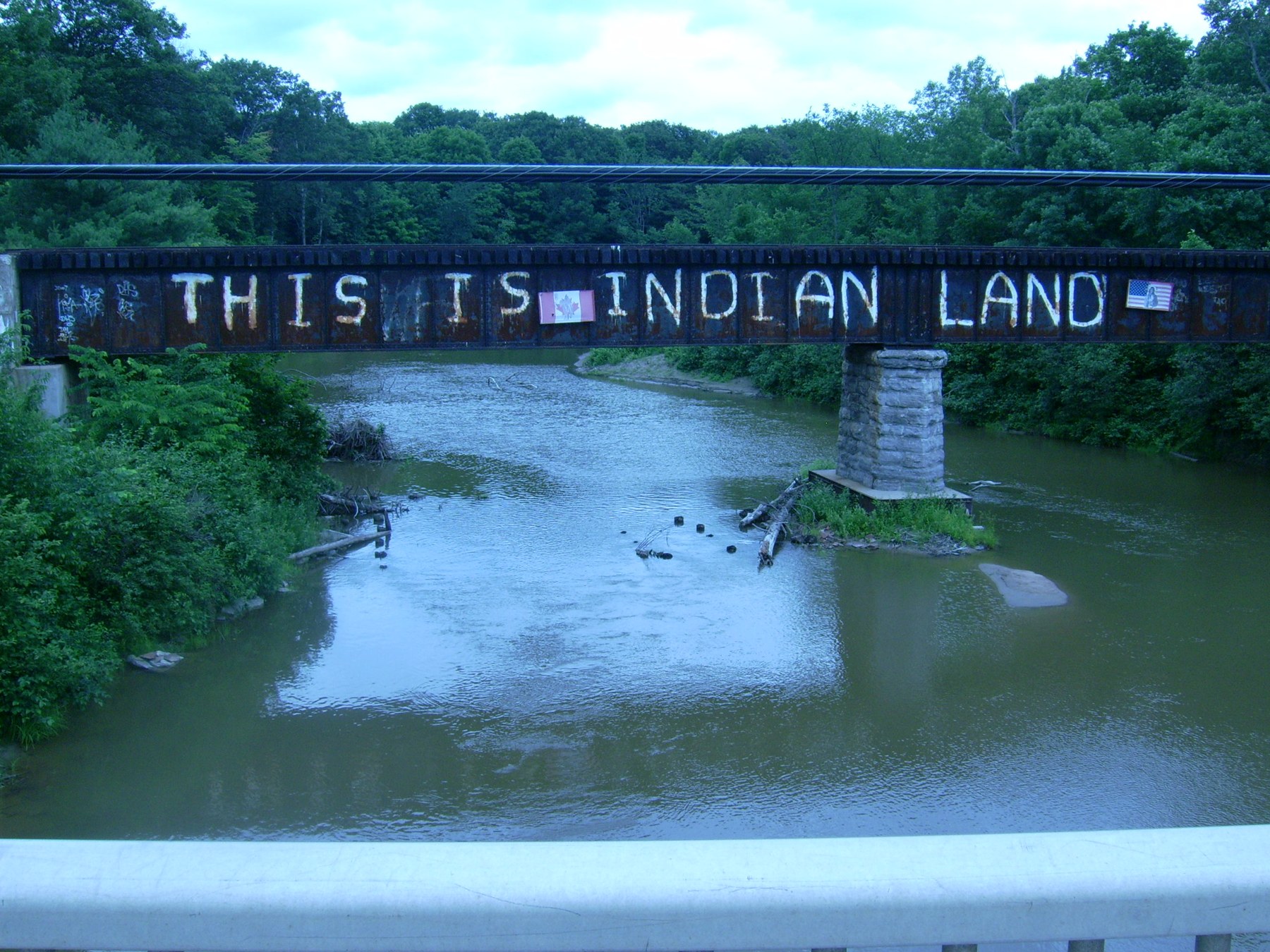 Rail bridge over the Garden River bearing the words “THIS IS INDIAN LAND”, with trees and water below.