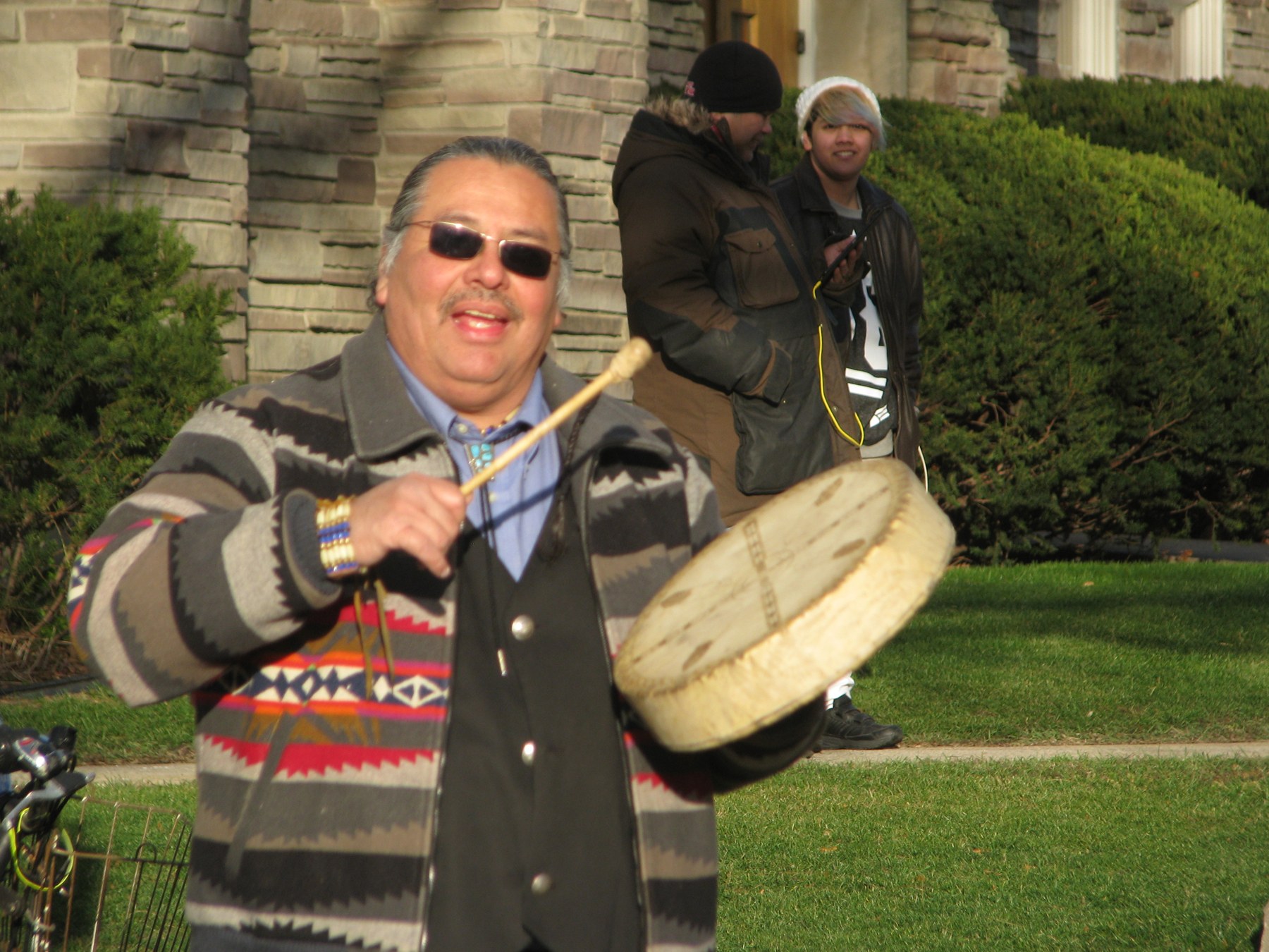 Myeengun Henry holding a hand drum outdoors at a public climate march in Waterloo in 2015.