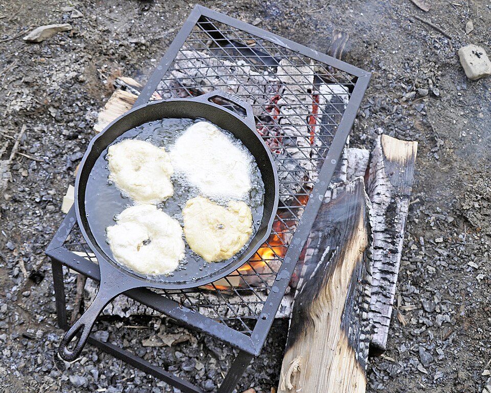 Full frame shows fry bread cooking in a cast-iron pan over a fire; no faces or private activities visible.