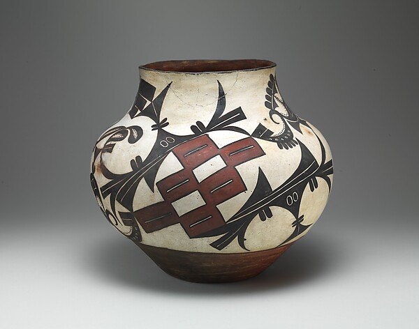 Full frame shows a painted ceramic jar on a neutral gray ground, including red, black and cream surface patterns.