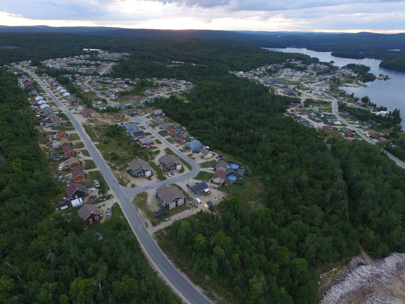 Aerial view of Manawan: houses and roads among forest beside a lake under a cloudy sky.
