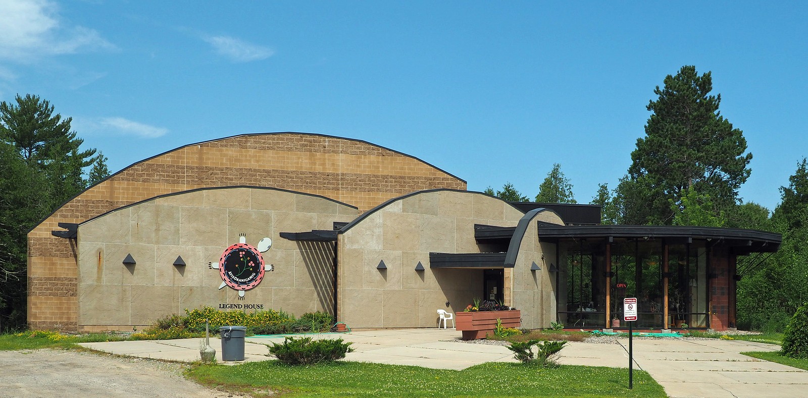 Full exterior view of the Bois Forte Heritage Museum, with its curved roof, Legend House sign, entrance and surrounding trees.