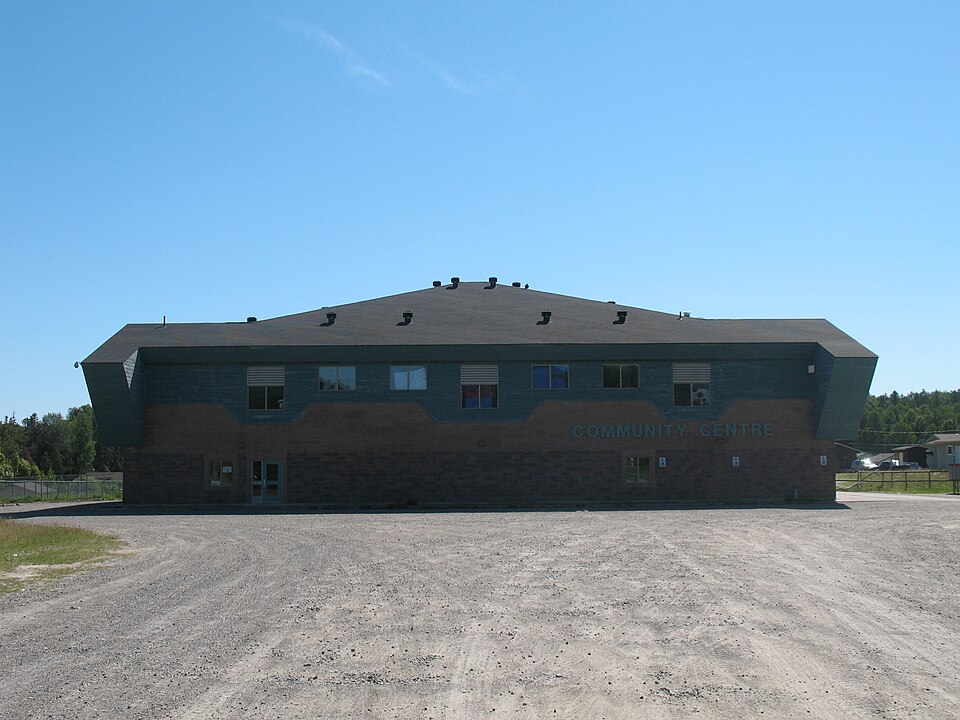 A broad two-storey community-centre building with a dark roof, windows and a gravel foreground, photographed at Whitefish Lake First Nation in 2010.
