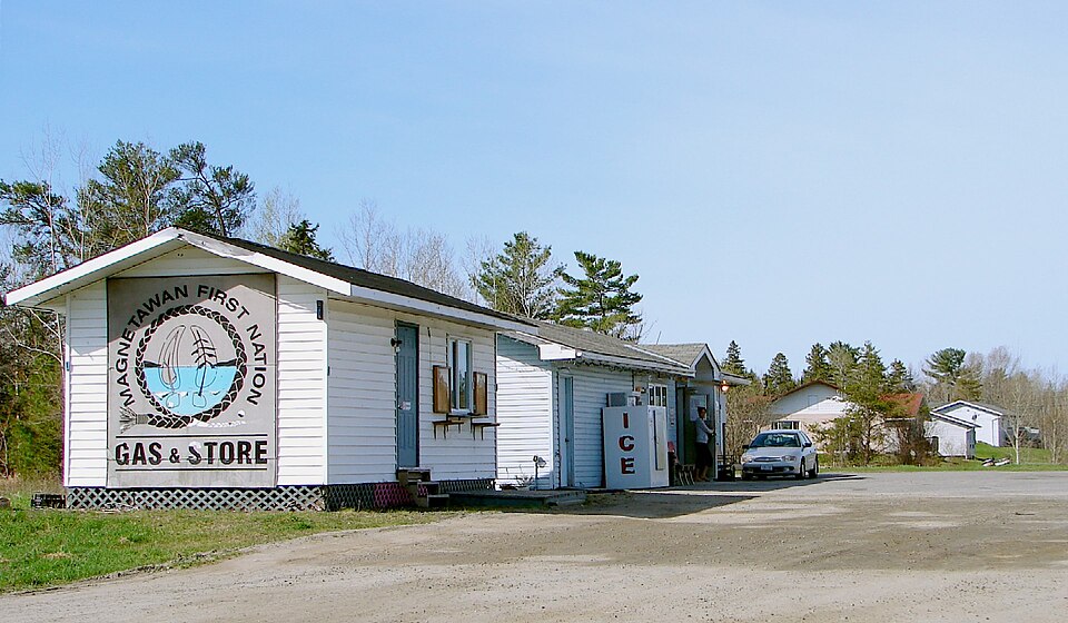 A white roadside building bearing a Magnetawan First Nation Gas & Store sign, with a parked vehicle and trees, photographed in May 2011.