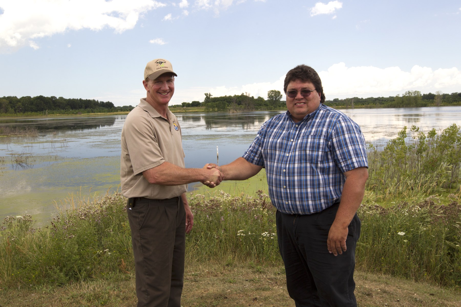 Biologist Gary van Vreede and a person identified by USFWS as an Oneida Tribe member shake hands beside a wetland.