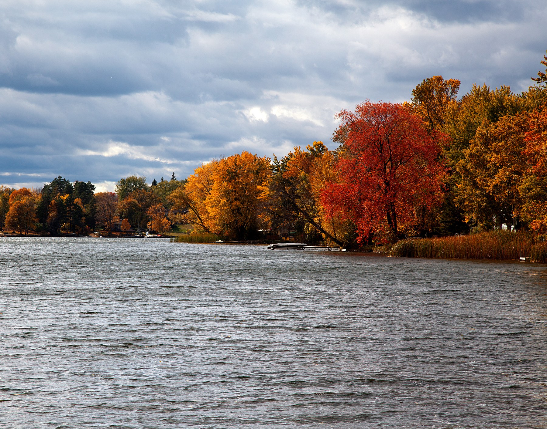 Waterfront with docks and autumn-colored trees beneath a cloudy sky.