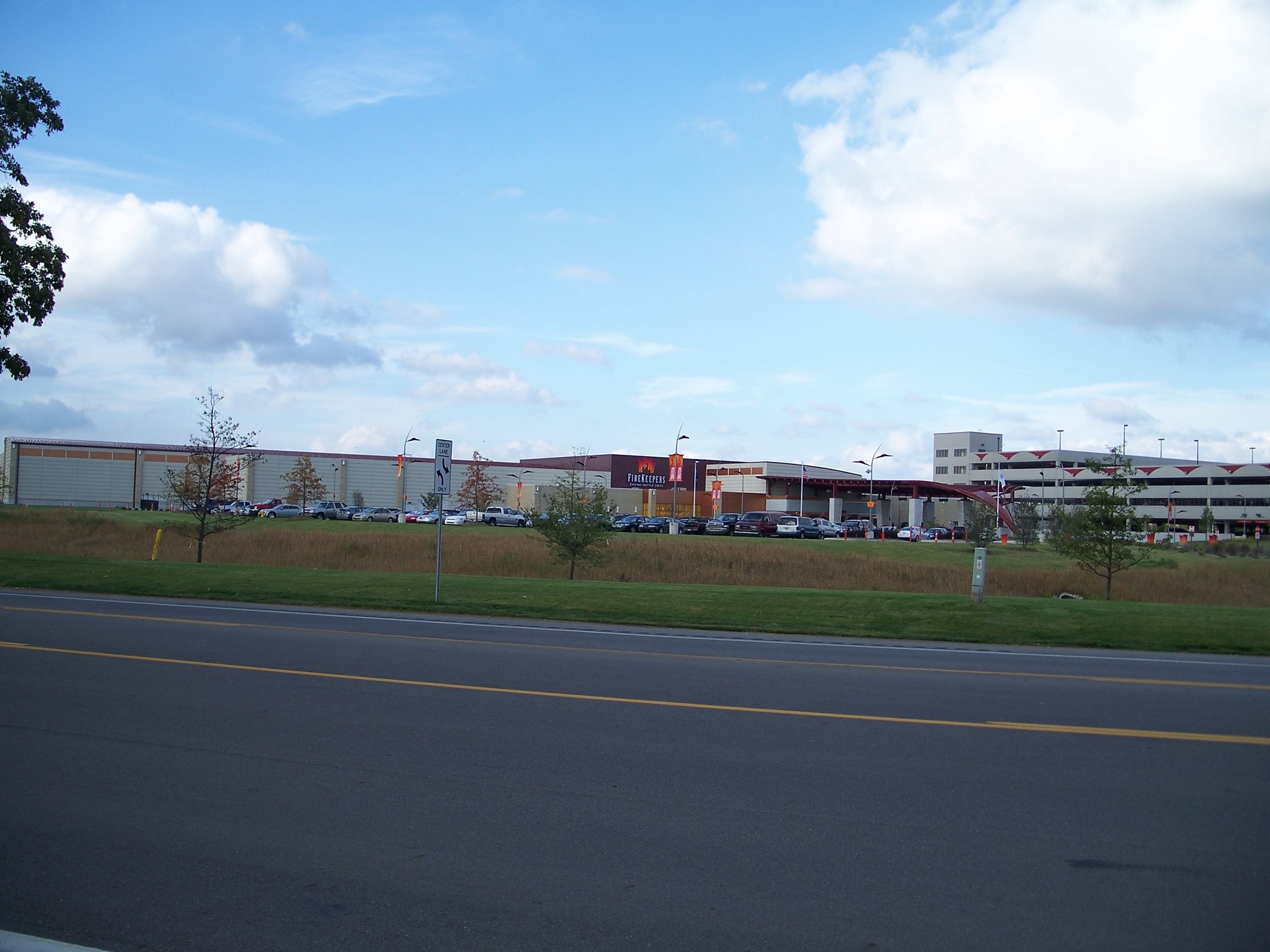 FireKeepers Casino building and parking structure beyond a roadway and grassy verge under a blue sky.