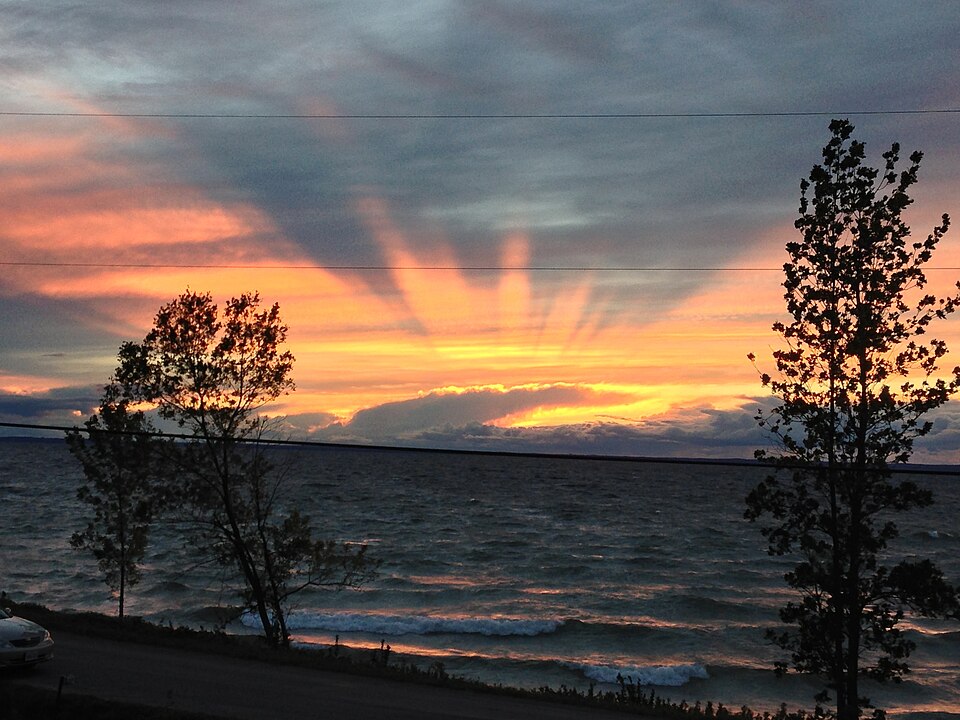 Sunset over water beside Georgina Island, with tree silhouettes, a roadside foreground and overhead utility wires.