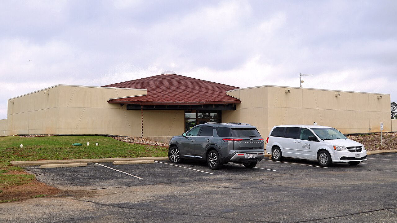 Exterior of the modern Caddo Mounds museum and visitor center, with two parked vehicles and cloudy sky.