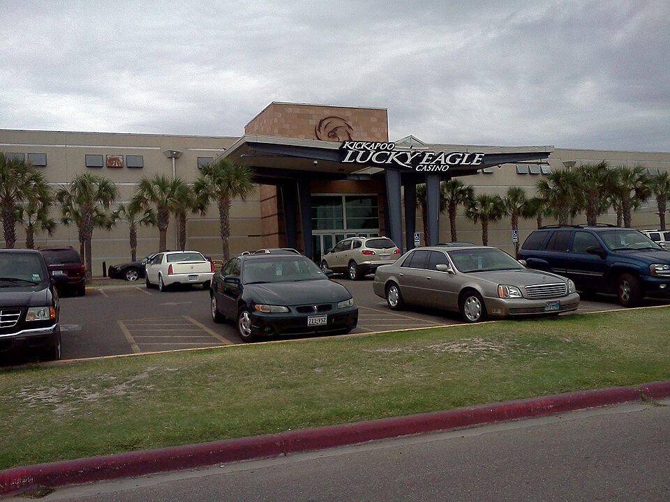The Lucky Eagle Casino entrance behind parked cars and palm trees beneath a cloudy sky.