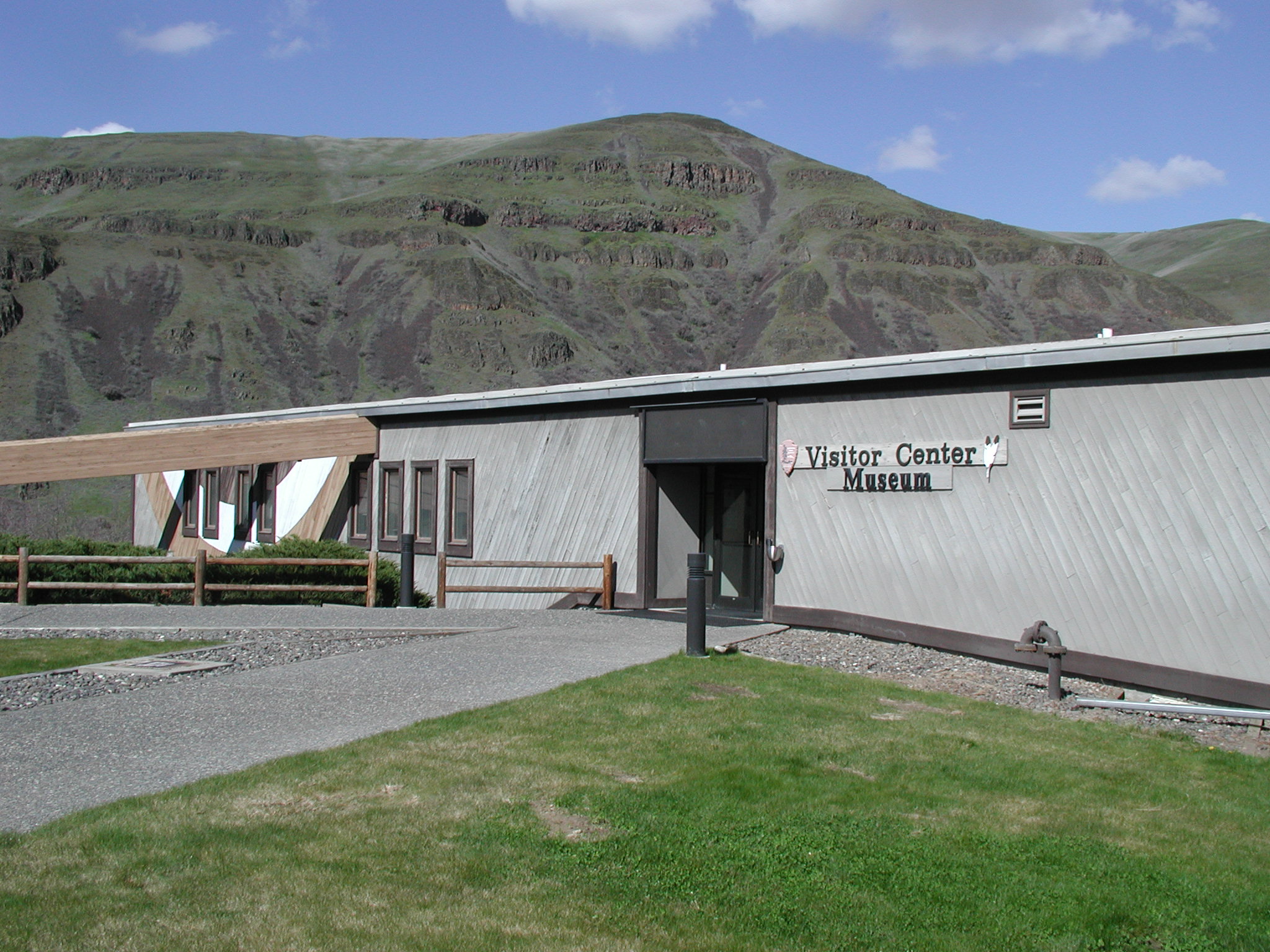 The low, wood-sided Spalding Visitor Center and Museum beneath green basalt hills.