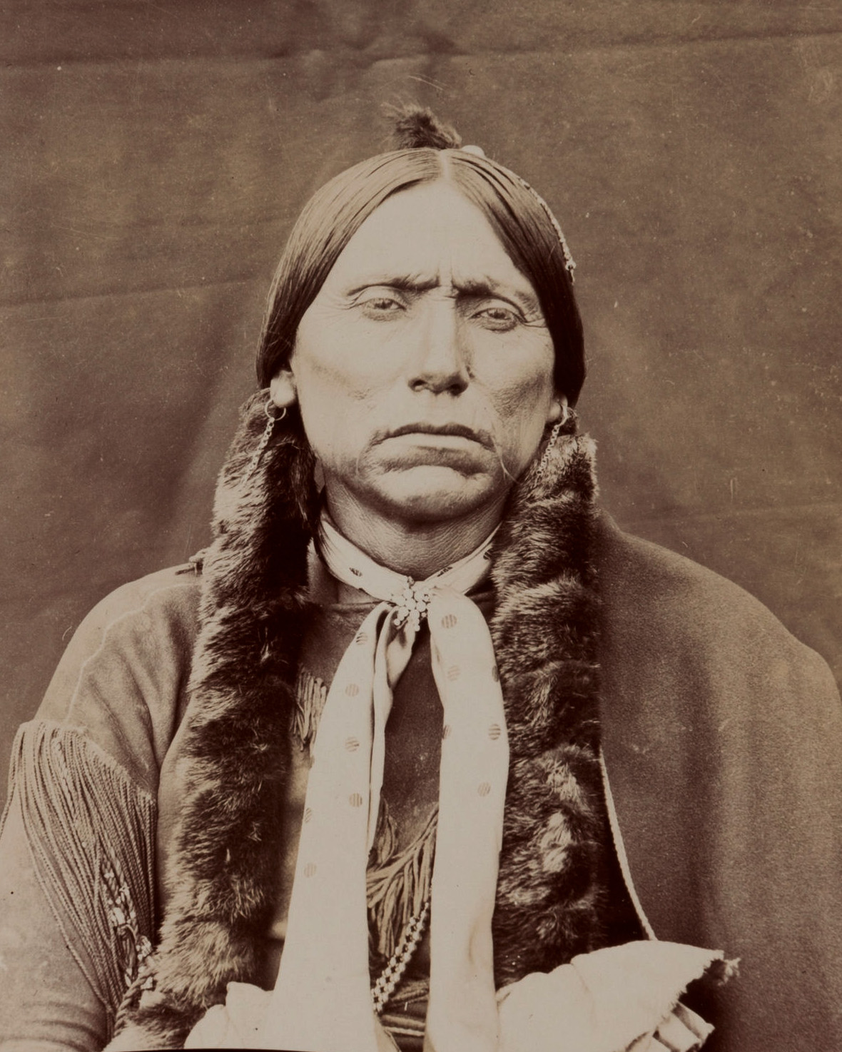 A sepia head-and-torso albumen portrait identified by its source as Quanah Parker, facing the camera against a cloth backdrop.