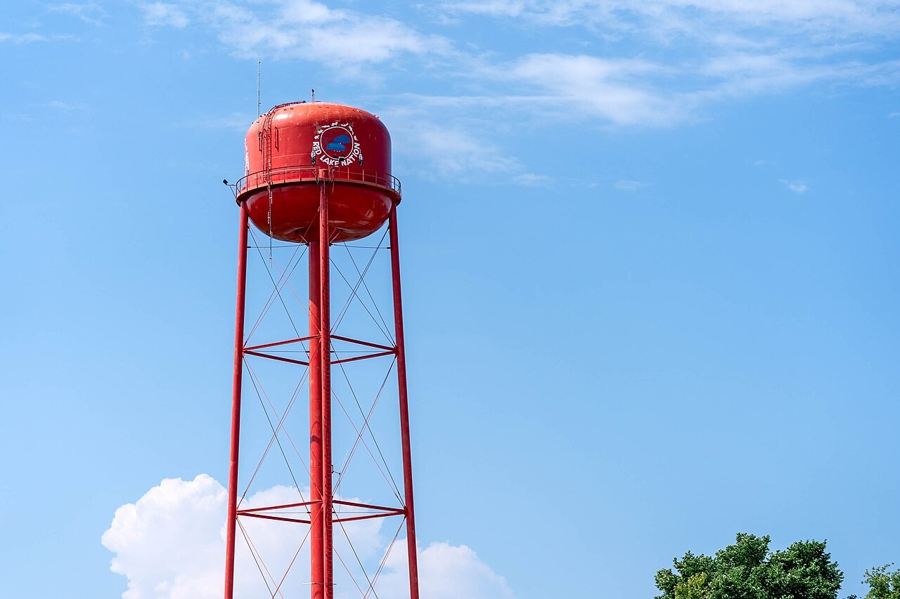 Red Lake Nation’s red water tower against a blue sky, with the full photographed frame and small portions of treetops below.