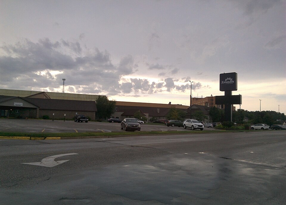 The Kewadin casino exterior and sign beyond a parking area, under a cloudy evening sky.