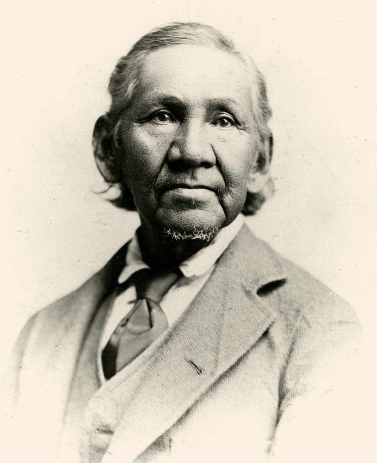 Historical black-and-white portrait of Simon Pokagon wearing a jacket and waistcoat.