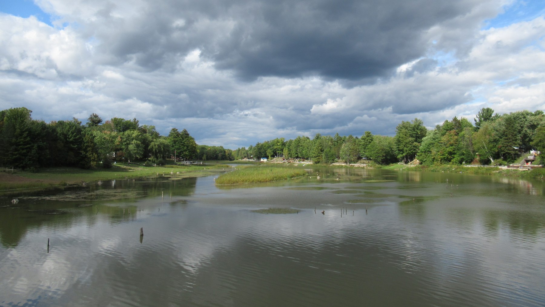 A modern view of the Tittabawassee River in Hay Township, Michigan, with tree-lined banks, a low vegetated island and cloud reflections.