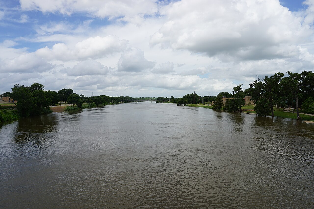 The Brazos River in modern Waco beneath cloudy skies, with bridges, trees and developed riverbanks.