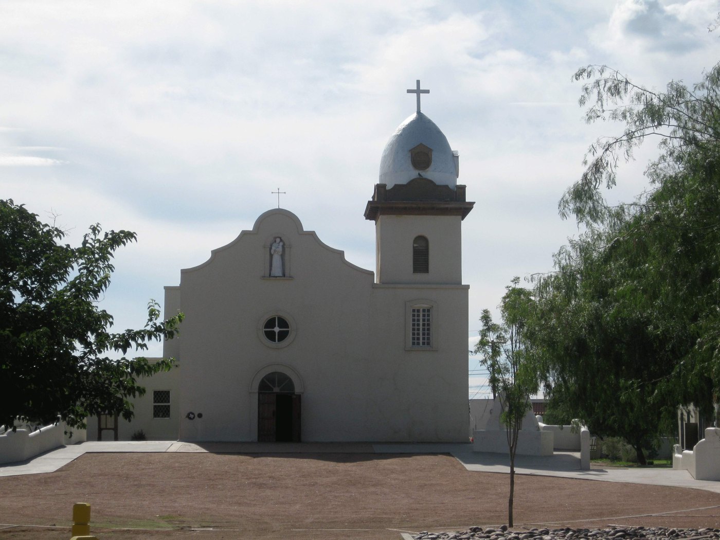 White facade and bell tower of Ysleta Mission in El Paso, framed by trees.